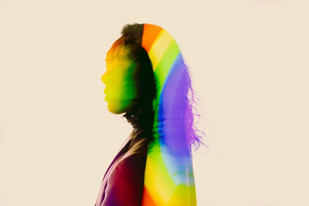 A person's in profile, partially in shadow and partially in rainbow colors.