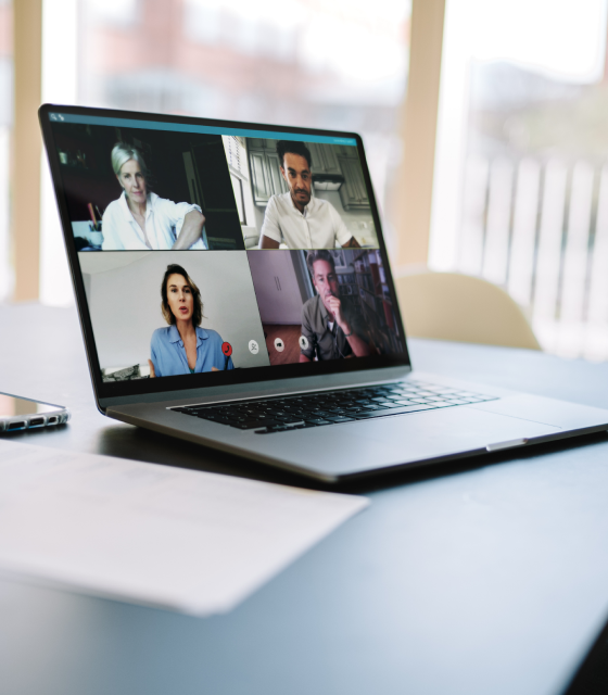 A laptop shows a virtual meeting in progress with four people in four separate rectangles.