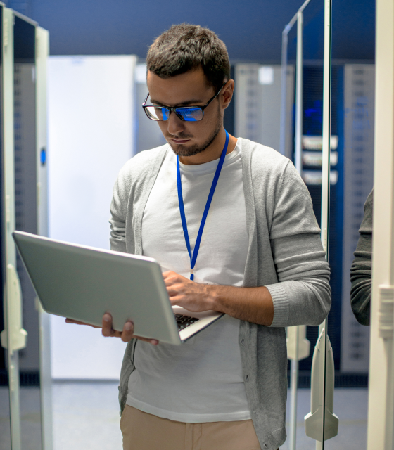 A man holds a laptop computer in a server room.