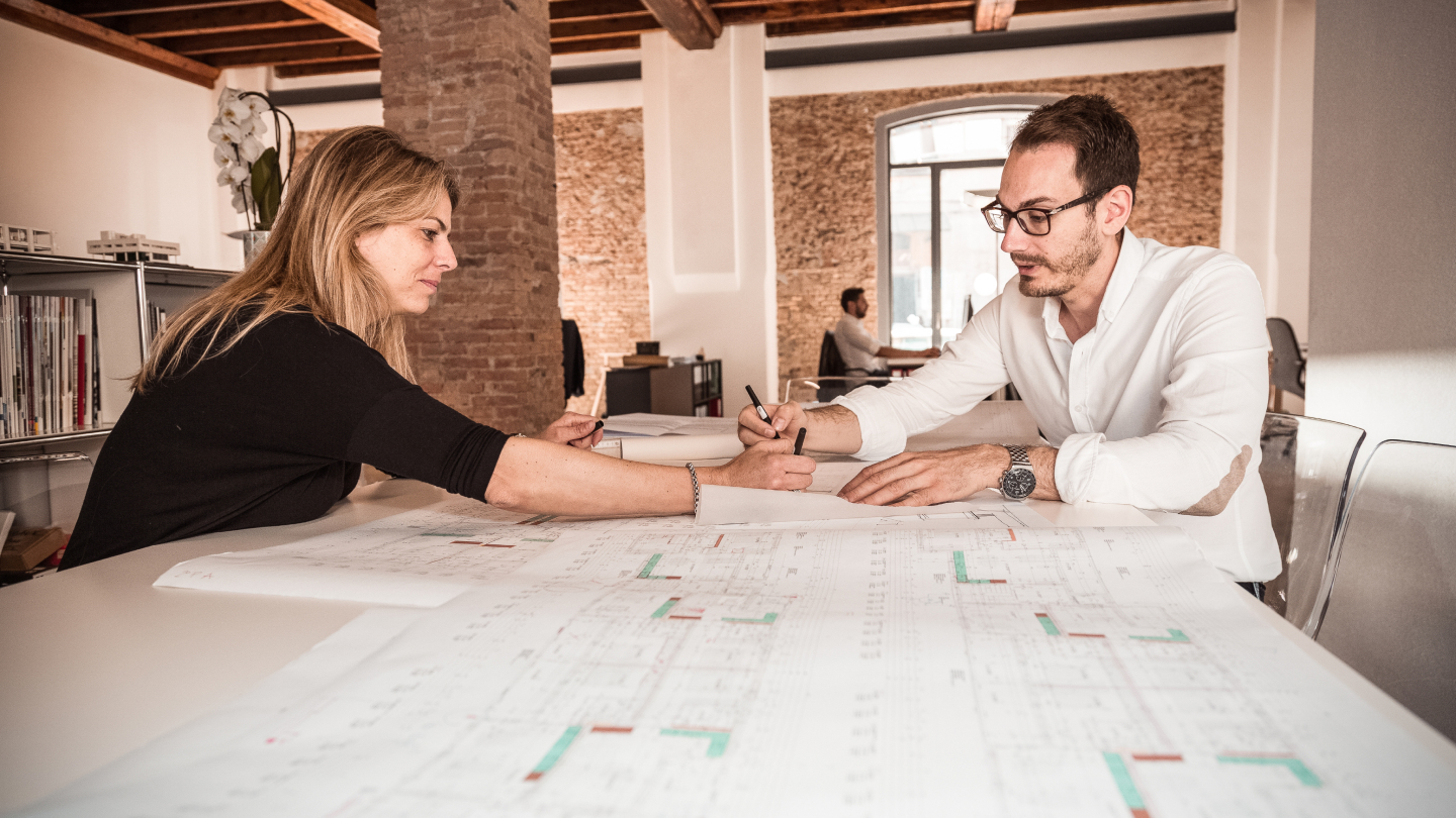 Two team members sit at a table and make notes on a large chart.