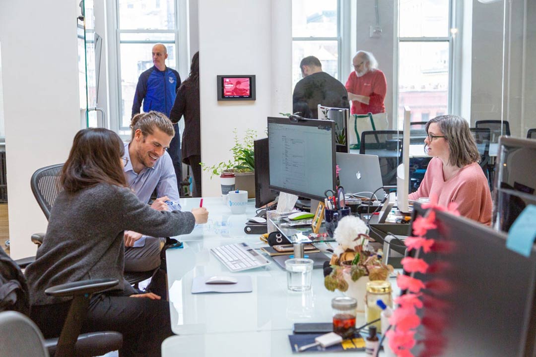 Office coworkers engaged in a discussion and work activities in a modern workspace.