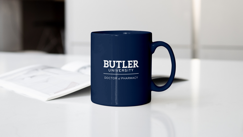 A dark blue coffee mug with Butler University branding on it sits beside an open notebook on a desk.