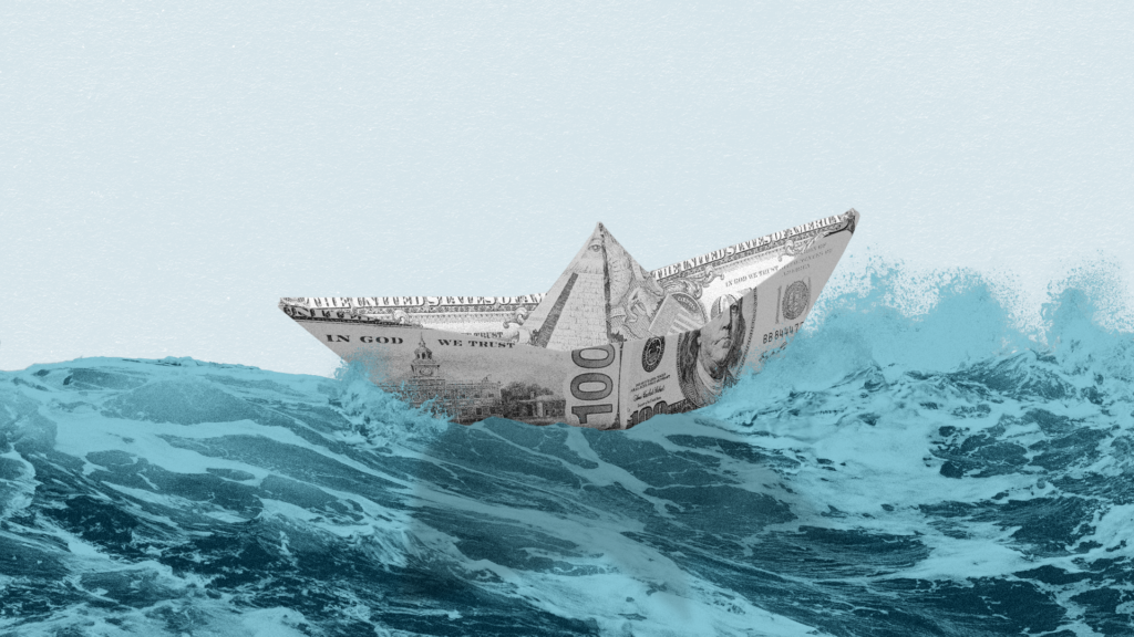 A hundred dollar bill folded into the shape of a boat rocks in the ocean waves.