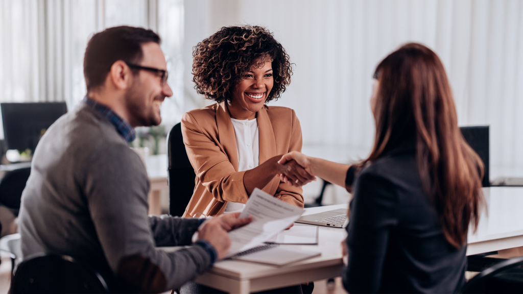 A small group of business colleagues meet over a conference table while two of the colleagues shake hands.