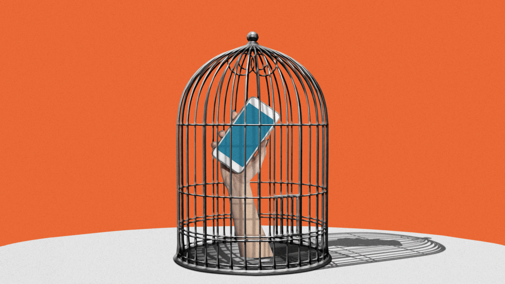 A hand holding a smart phone is enclosed within a birdcage.