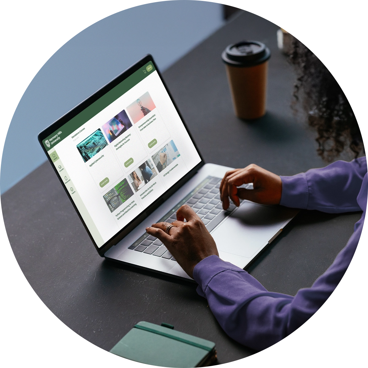 A closeup of hands typing on a laptop beside a coffee cup and a notebook.